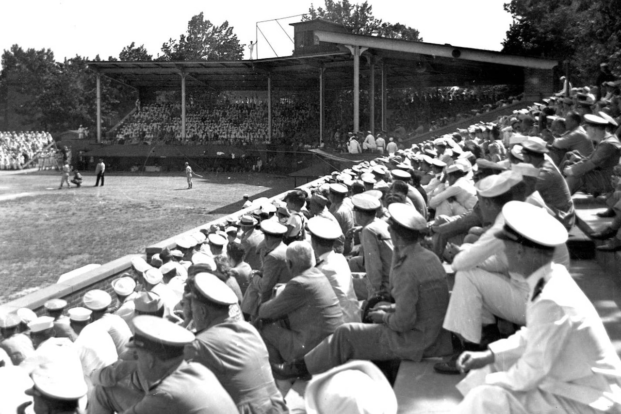 Fans sit in the stands and watch a baseball game.