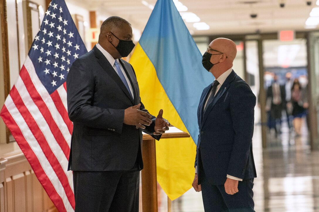 Secretary of Defense Lloyd J. Austin III stands and converses with another man in a hallway.