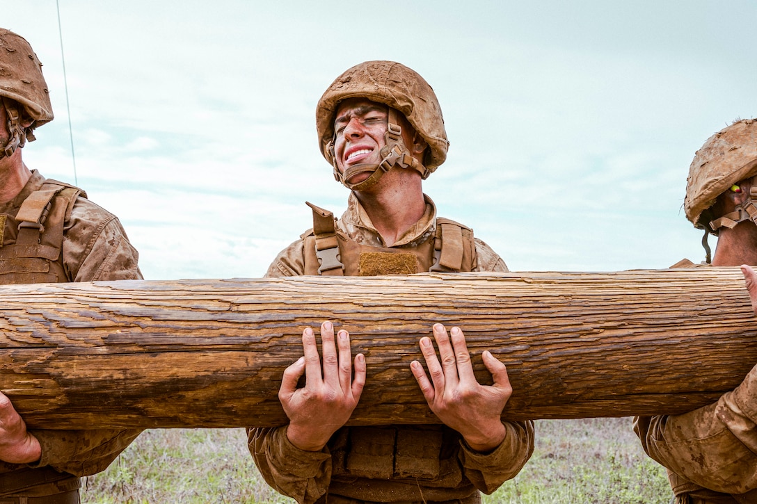 A Marine grimaces while holding up a log.