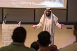 Kuwaiti in white headress and garb stands in front of audience giving a presentation