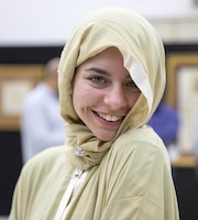 Young woman in tan and white robe and head covering smiles.