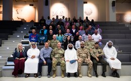 Group of Soldiers, Civilians, and Kuwaitis sit on benches in a room with maps and arabic script on the walks