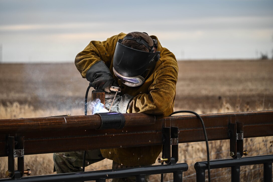 An airman works on a fence in a large field.