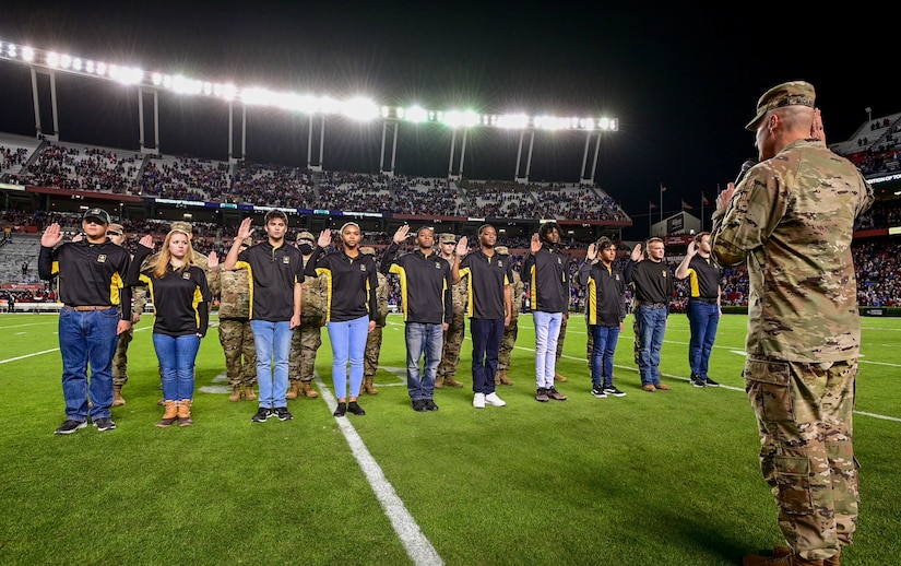 group of young men and women holding up their right hand on a football field.