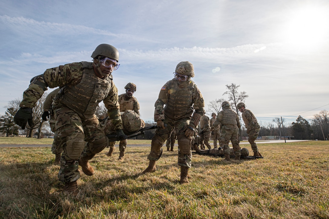 Two soldiers carry a simulated patient on a stretcher.