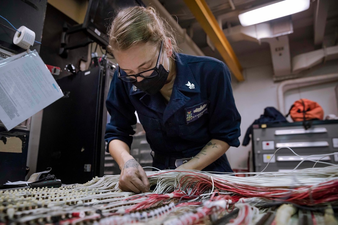 A sailor works with wiring in an electrical panel.