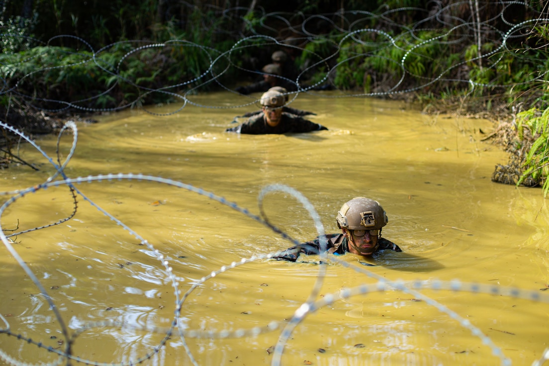 Marines walk through deep muddy water.