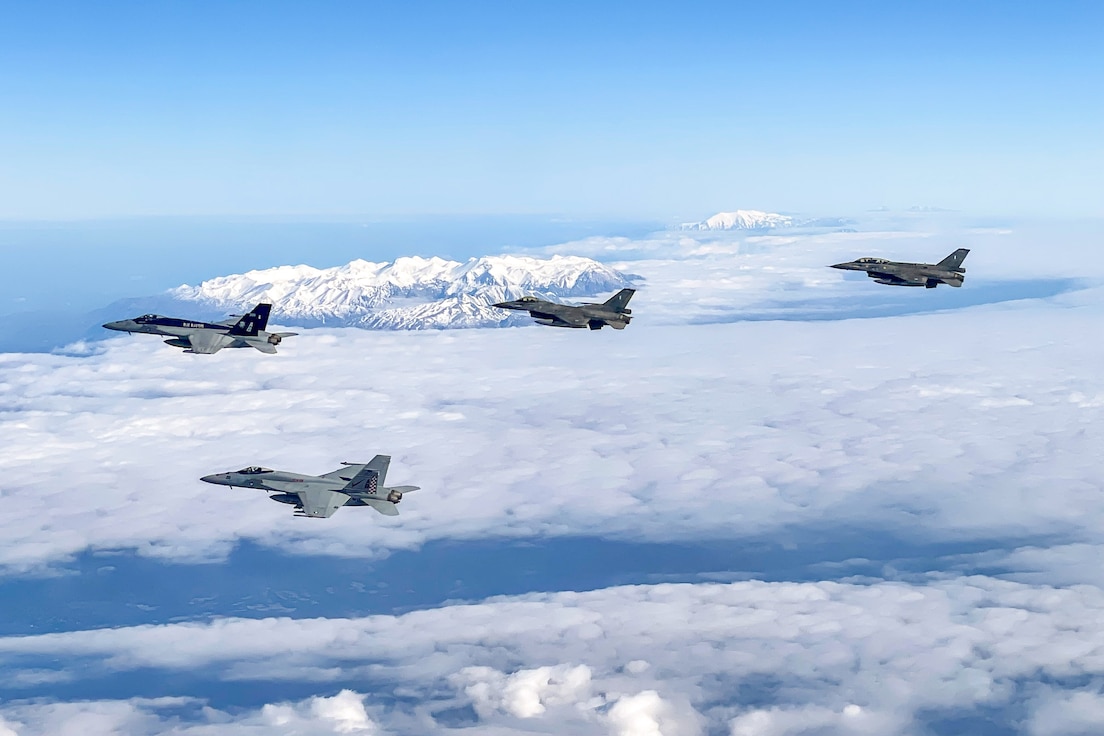 Four fighter jets fly above the clouds.