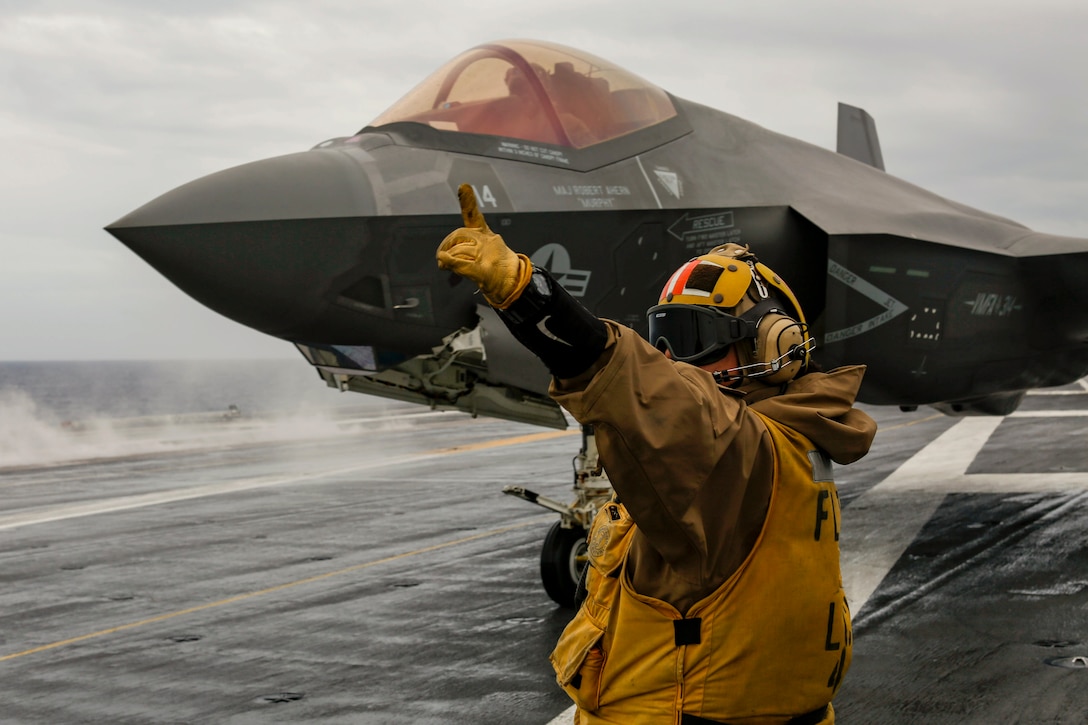 A sailor signals to an aircraft aboard a ship at sea.