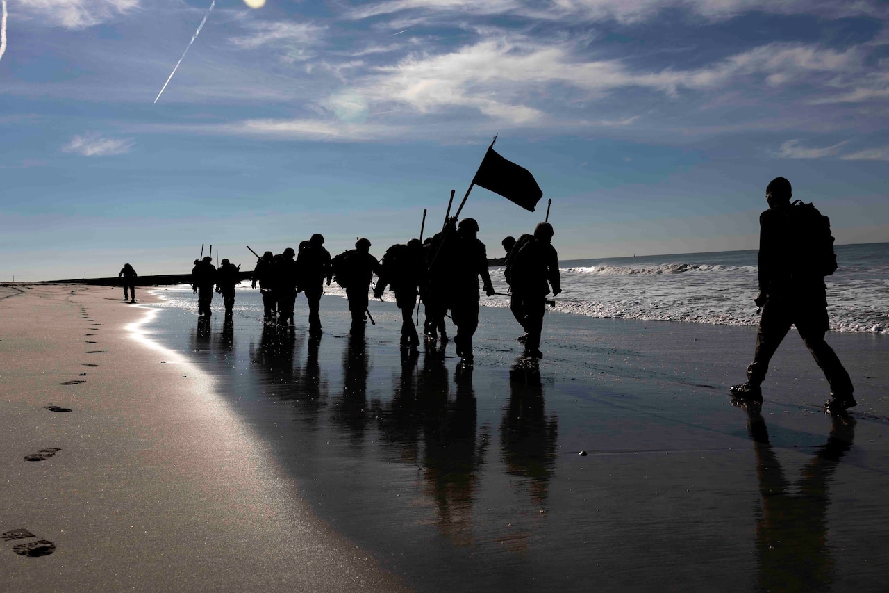 A group of Marines march on a beach.