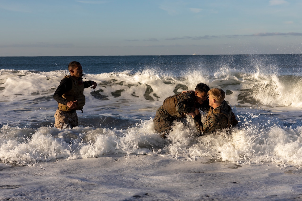Two Marines grapple in the ocean as another Marine watches.