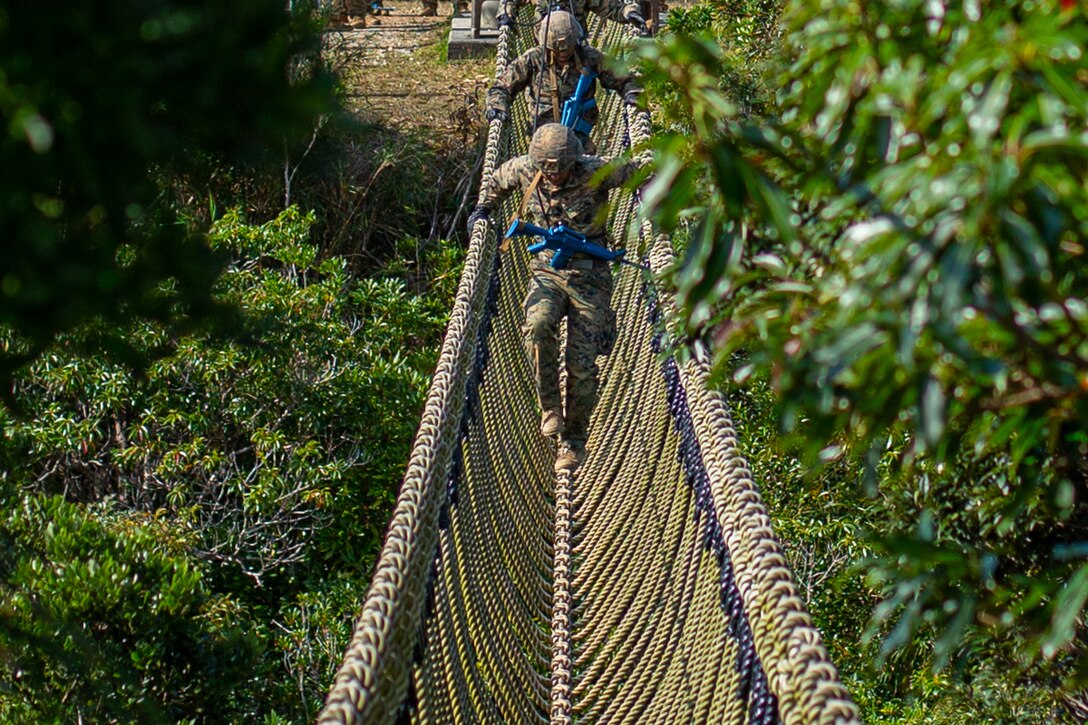 Three Marines walk across a rope bridge in a jungle.