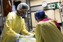 Two medical personnel in a hospital setting wearing personal protective equipment look down at something off camera.