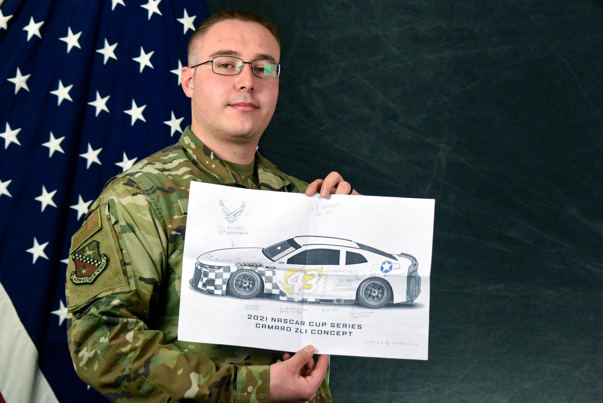 A man in Air Force uniform holding a drawing in front of a flag.