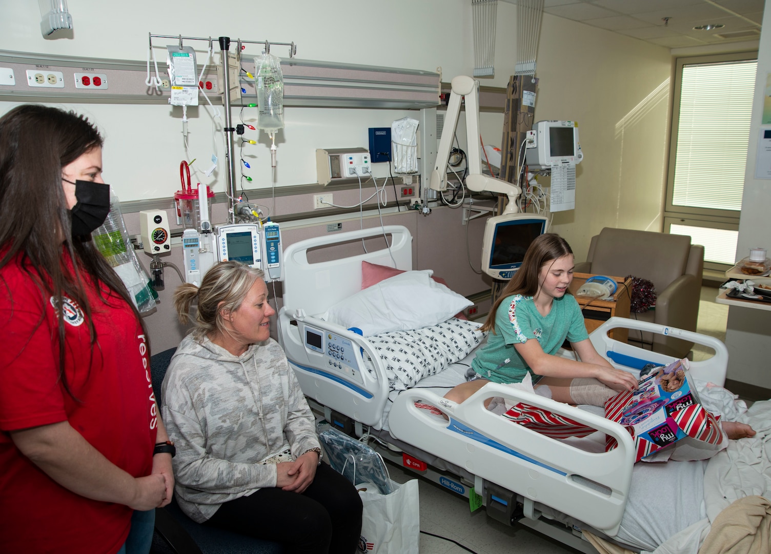 PORTSMOUTH, Va. (Dec. 15, 2021) – Addys Vasquez (left), an Operation Homefront volunteer, gifts a present an NMCP patient and her mother, Dec. 15. Operation Homefront is a national nonprofit whose mission is to build strong, stable, and secure military families so they can thrive — not simply struggle to get by — in the communities they have worked so hard to protect. (U.S. Navy photo by Mass Communication Specialist 3rd Class Ariana Torman/Released)