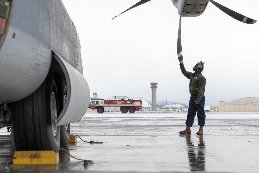 A Marine stands on the tarmac and inspects a propeller.