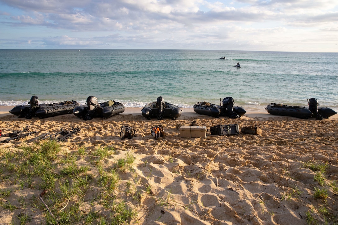 Five rubber rafts sit next to each other on a beach.