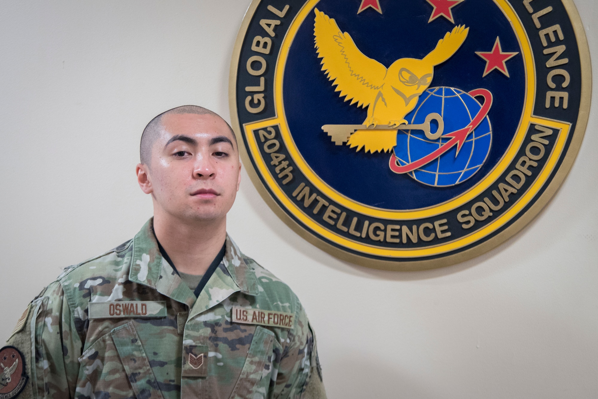 New Jersey Air National Guard Staff Sgt. Joseph Oswald stands in front of the 204th Intelligence Squadron's emblem located in the 108th Operations Group building on Joint Base McGuire-Dix-Lakehurst, N.J., Jan. 9, 2022.