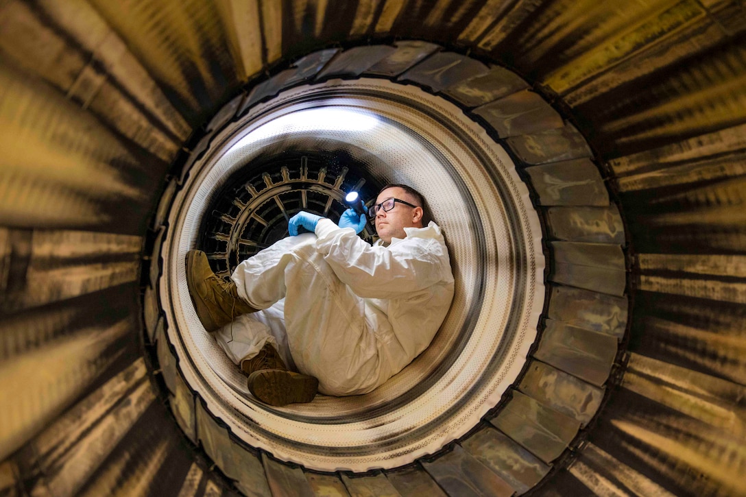 An airman inspects the inside of a jet engine with a flashlight.