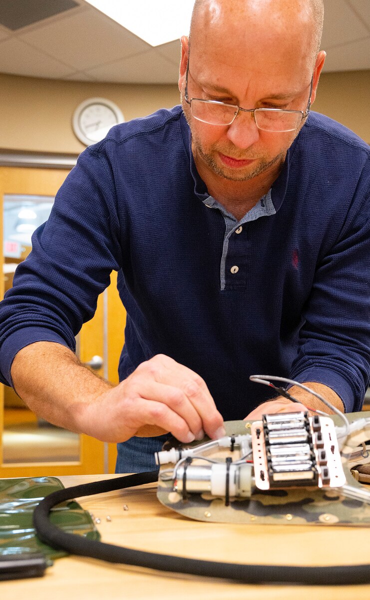 Matthew Sunday, an engineer with the Wright Brothers Institute’s Rapid Innovation Program, works on placing the battery compartment in the liquid-cooled plate carrier prototype Dec. 1, 2021, at his lab in Riverside, Ohio. The system uses a small pump to circulate drinking water and cool service members wearing body armor. (U.S. Air Force photo by R.J. Oriez)