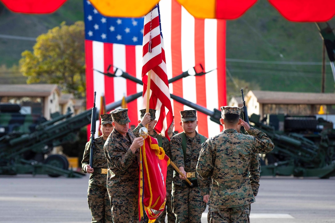 Marines stand in a huddle; some holding flags and others holding weapons.