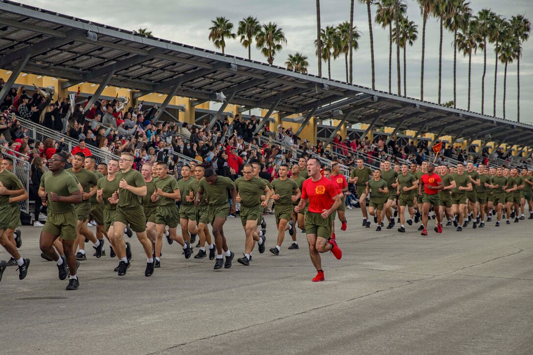 Marines run in formation in front of an audience.