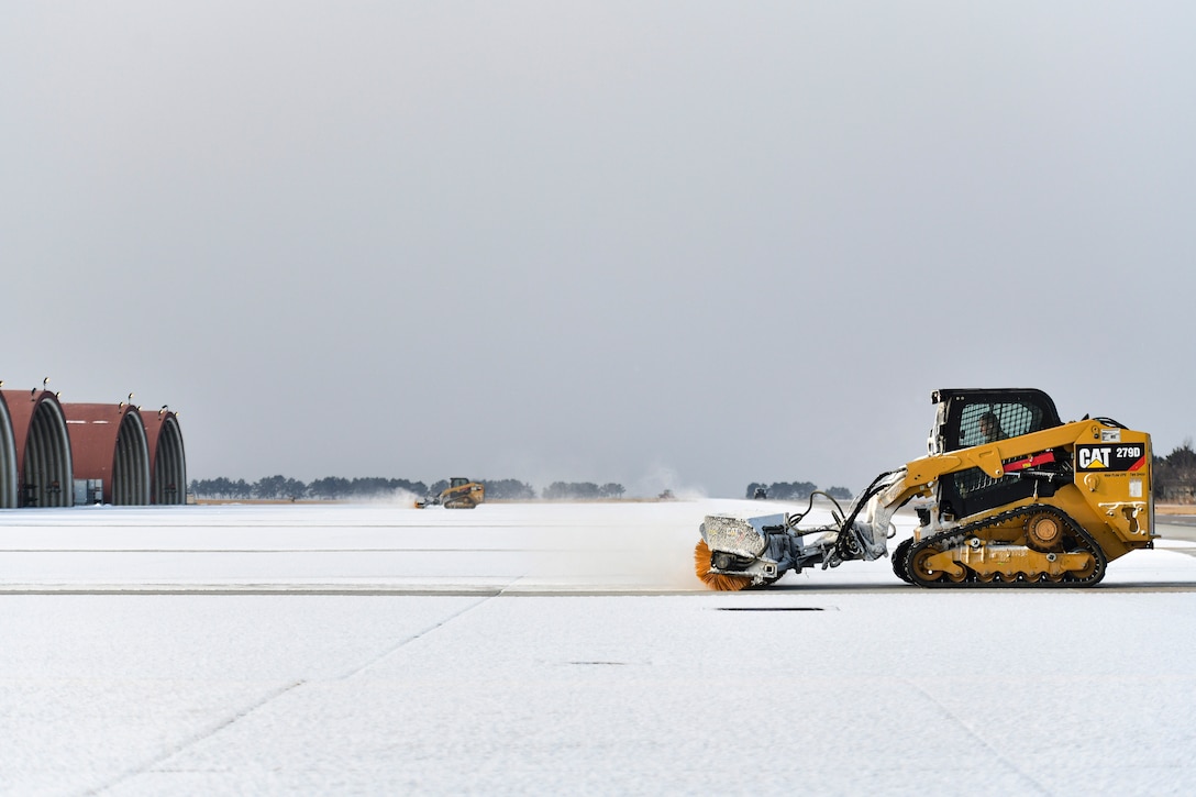 Airmen use combat track loaders to remove snow at an airfield.