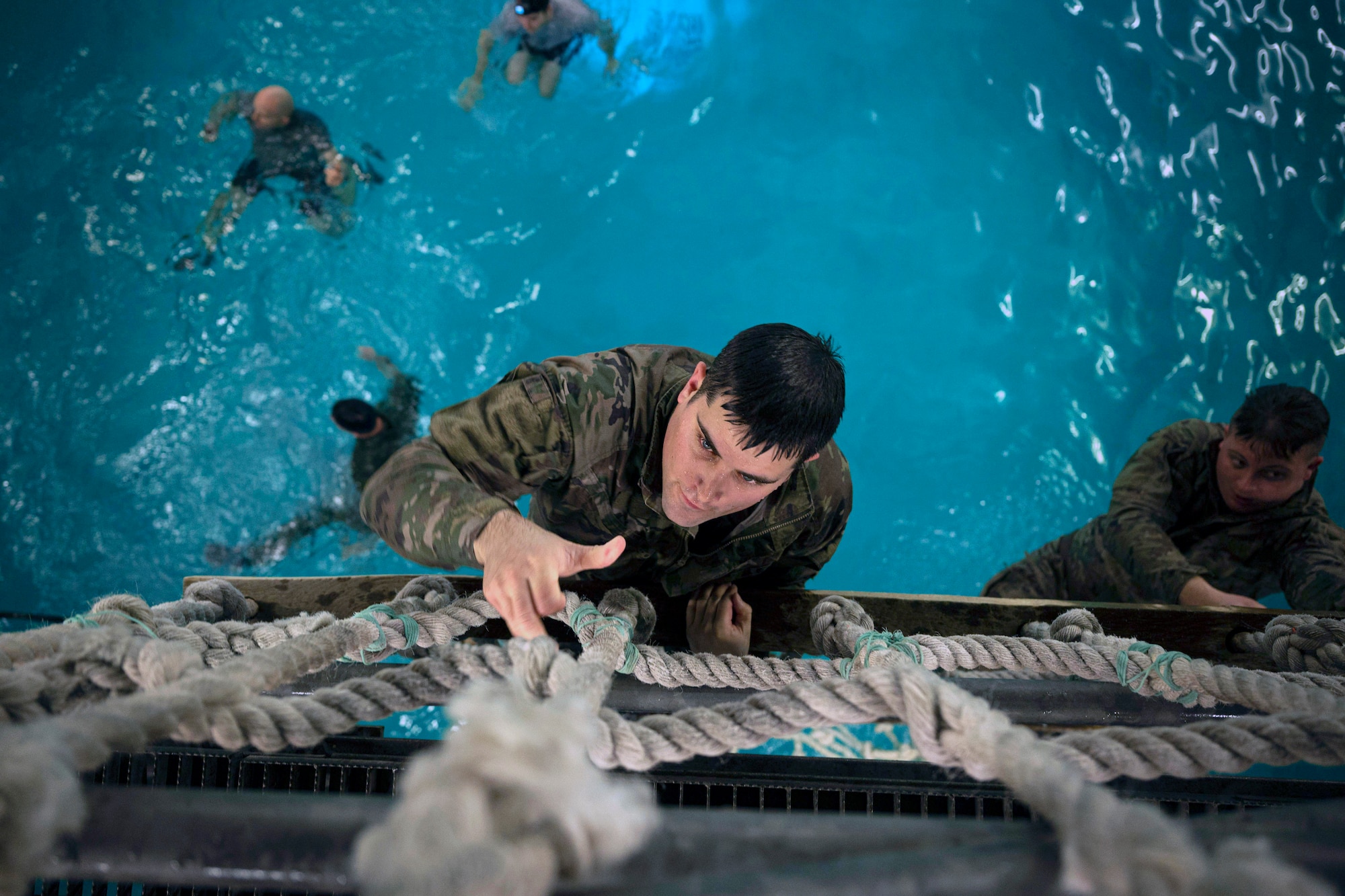 Tech. Sgt. Tyler Cameron climbs a rope ladder over a pool