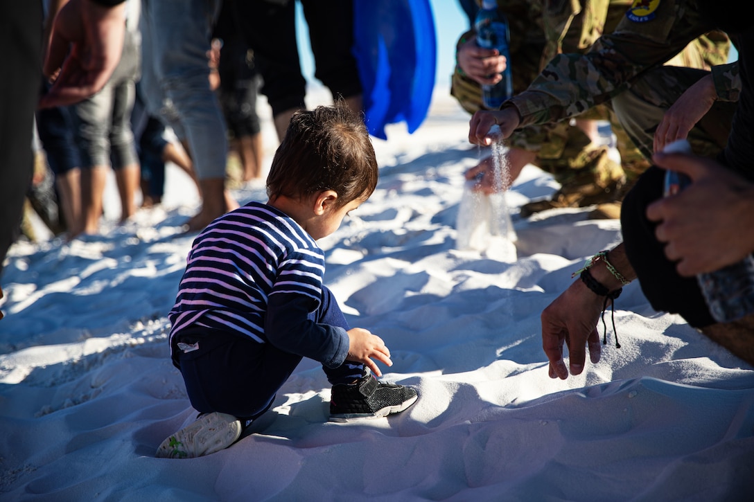 An Afghan child plays in the sand with soldiers.