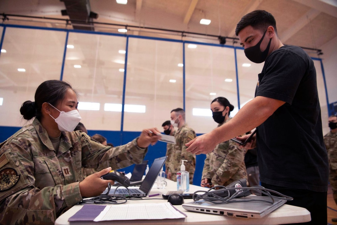 An Air Force officer wearing a face mask hands an ID card back to an airman wearing a face mask.