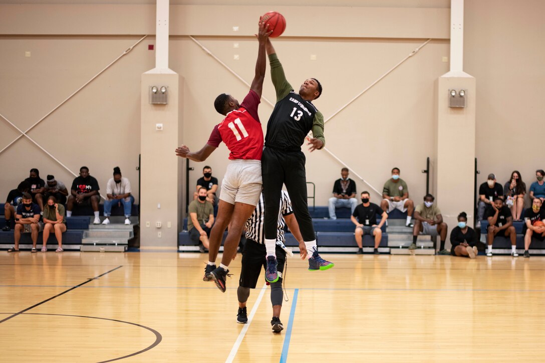 A sailor jumps during a tip-off of a basketball game as an audience watches.