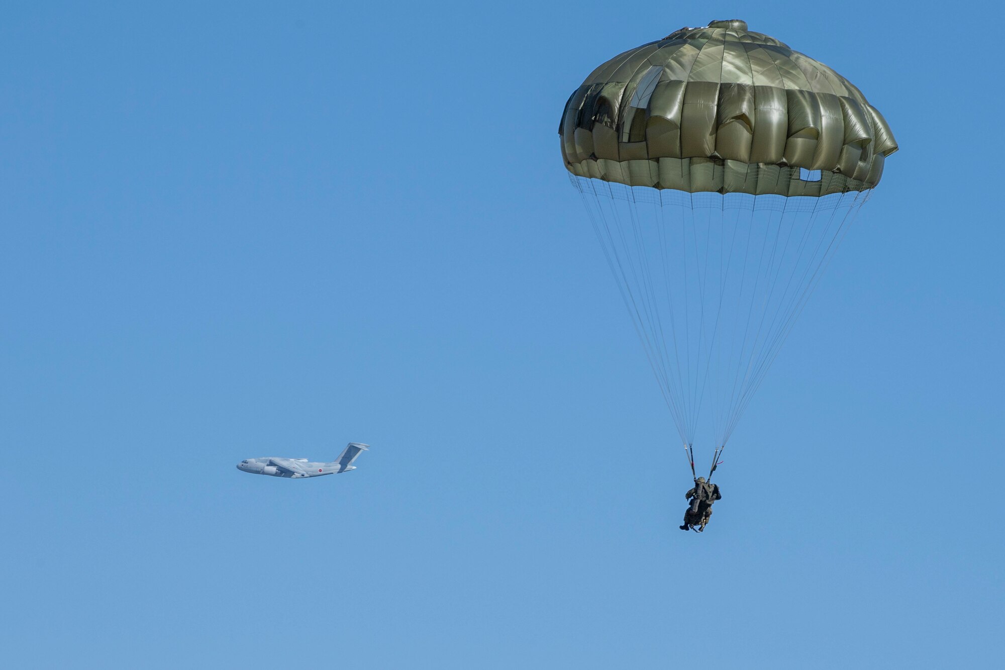 A Japan Air Self-Defense Force C-130H Hercules flies past a Japan Ground Self-Defense Force paratrooper