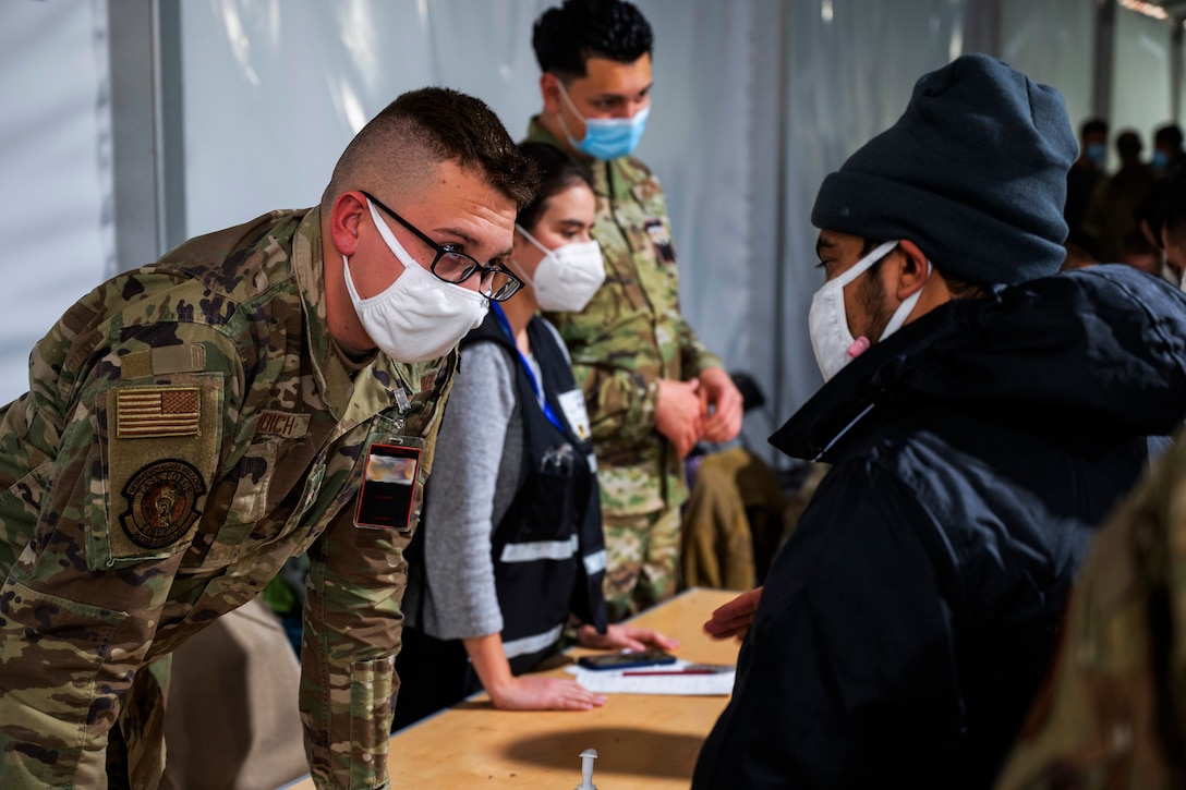 An airman, wearing a face mask, speaks to an Afghan guest during an event.