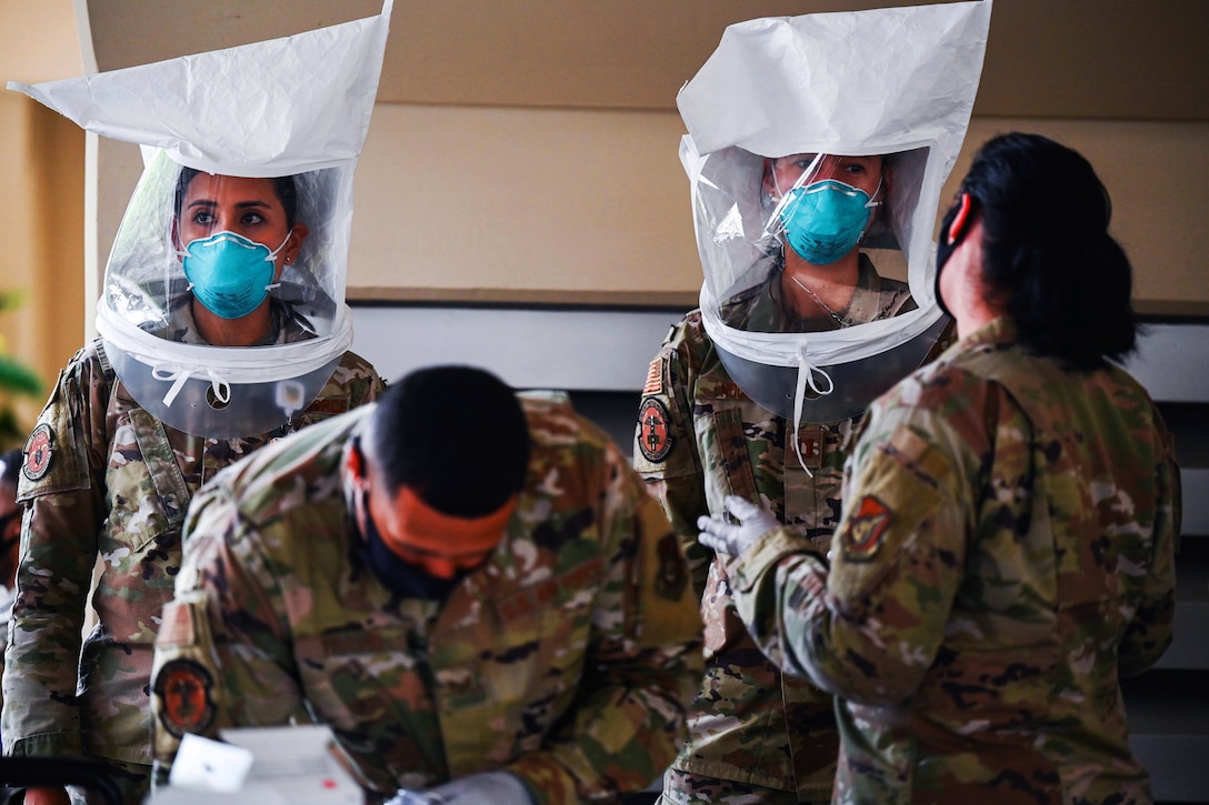 Two airmen perform N95 mask fit tests while one airman monitors them, and another bends over to record their response.