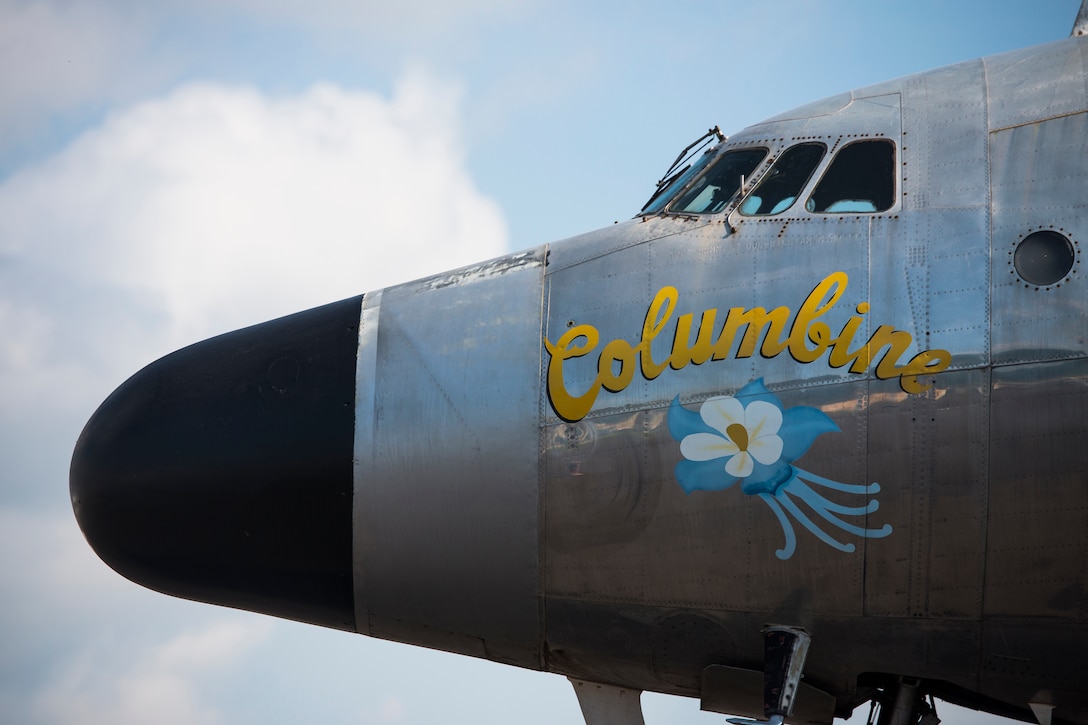 The nose of an airplane has the word "Columbine" and a flower painted on it.