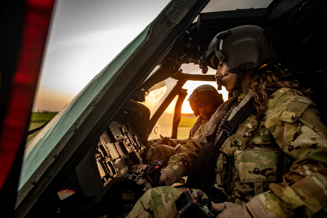 Two pilots sit at the controls of a helicopter.