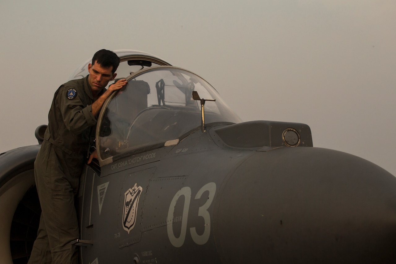 A pilot stands on the ladder outside the cabin on his fighter jet.