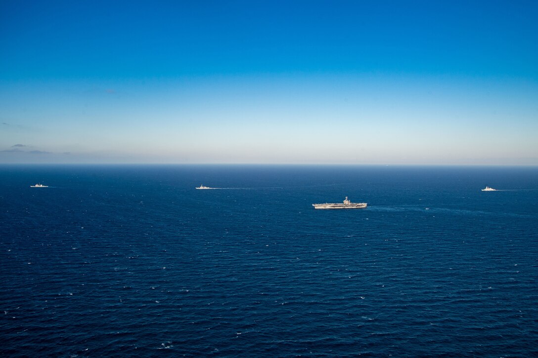 Four military ships sail across a wide open ocean.