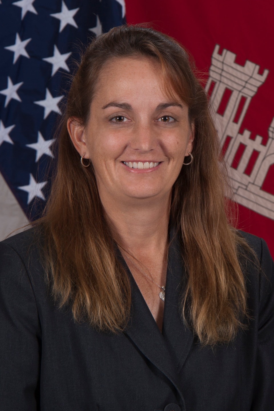 Dr. Jackie Pettway smiles in her official headshot in front of the American and USACE flags.