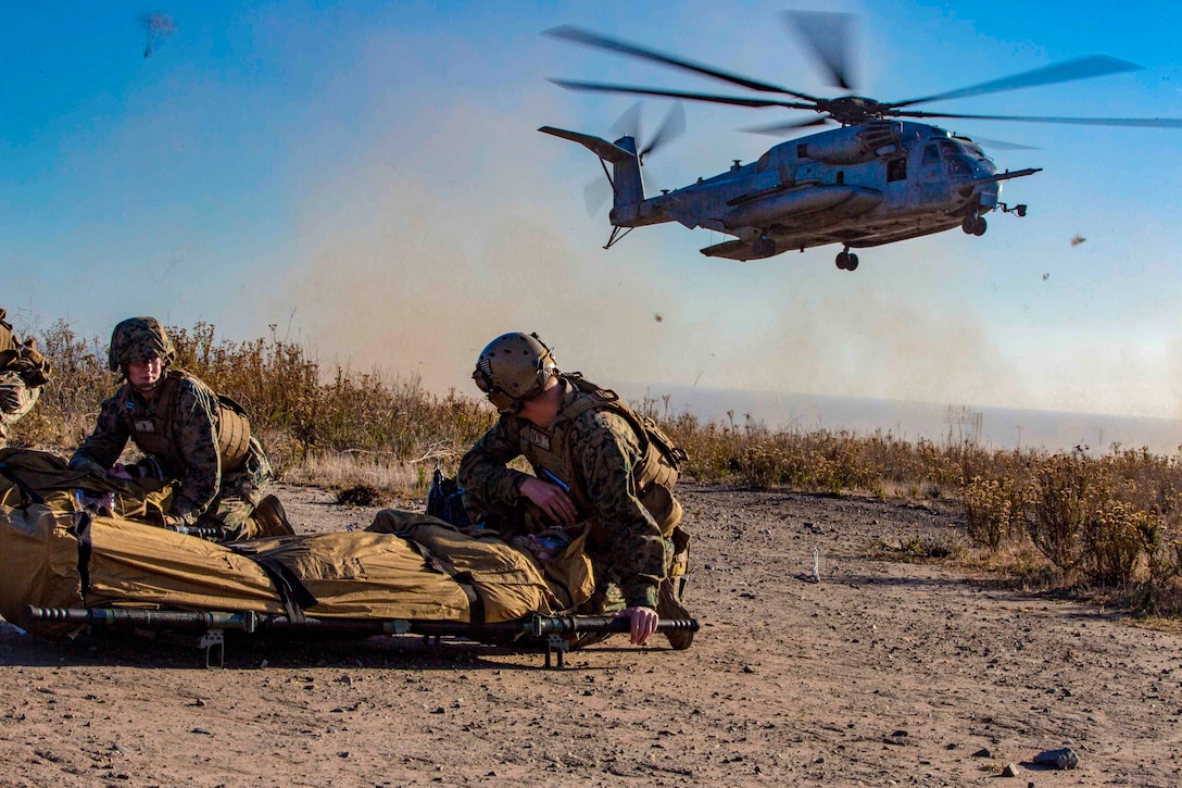 Sailors shield simulated patients as a helicopter prepares to land.