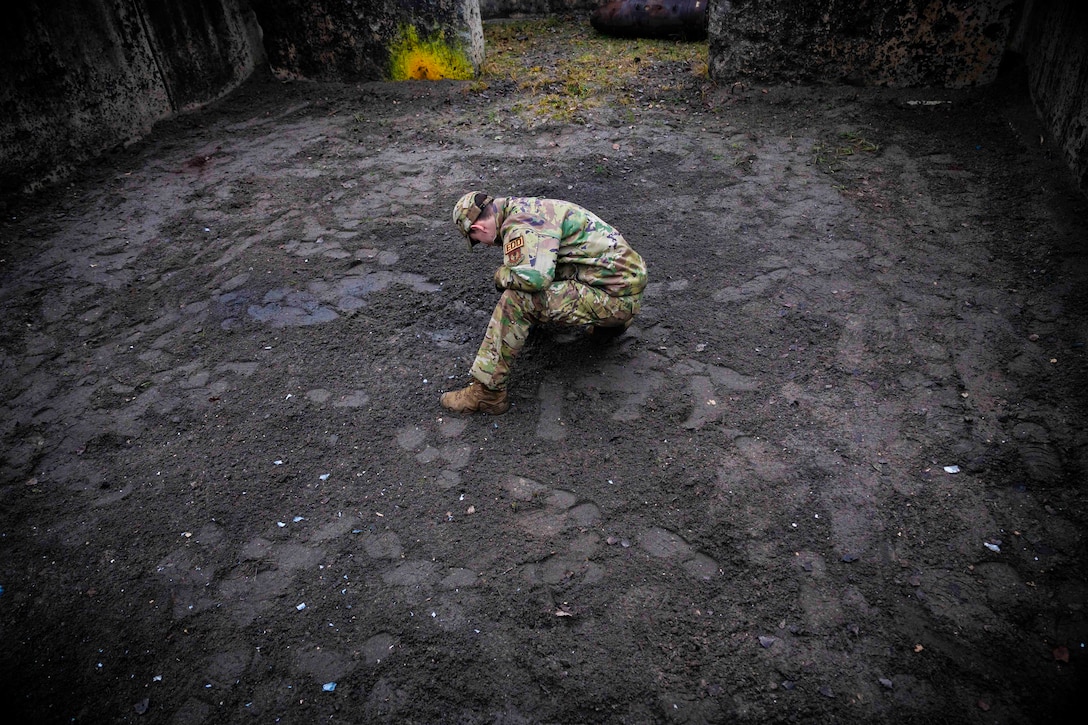 An airman gathers shrapnel on the ground.