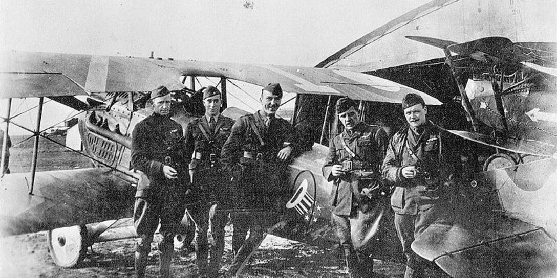 Five soldiers pose for a photo in front of an aircraft.