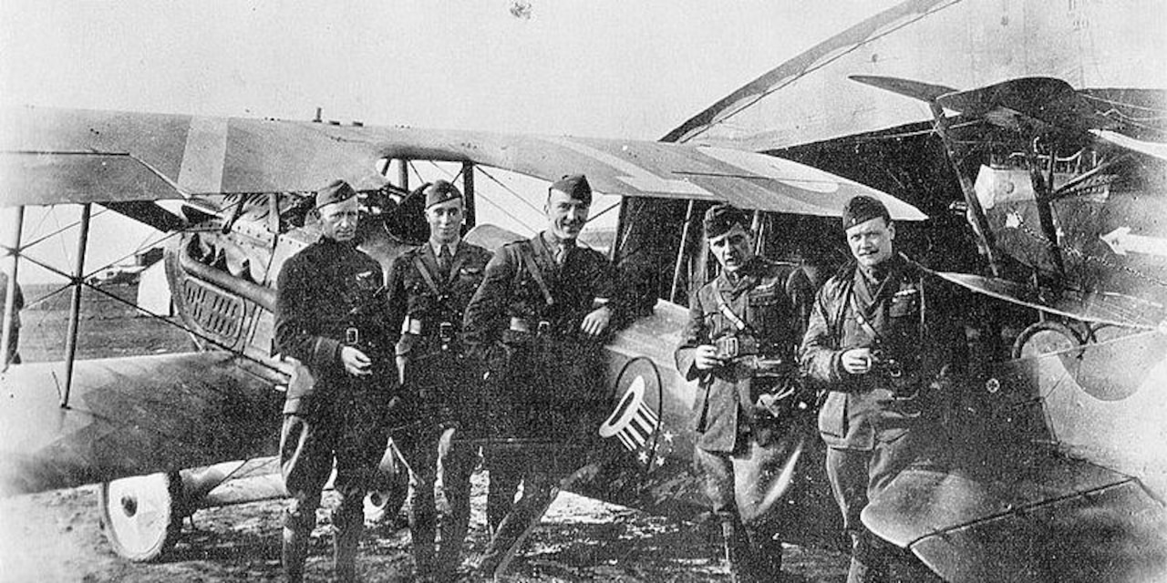 Five soldiers pose for a photo in front of an aircraft.