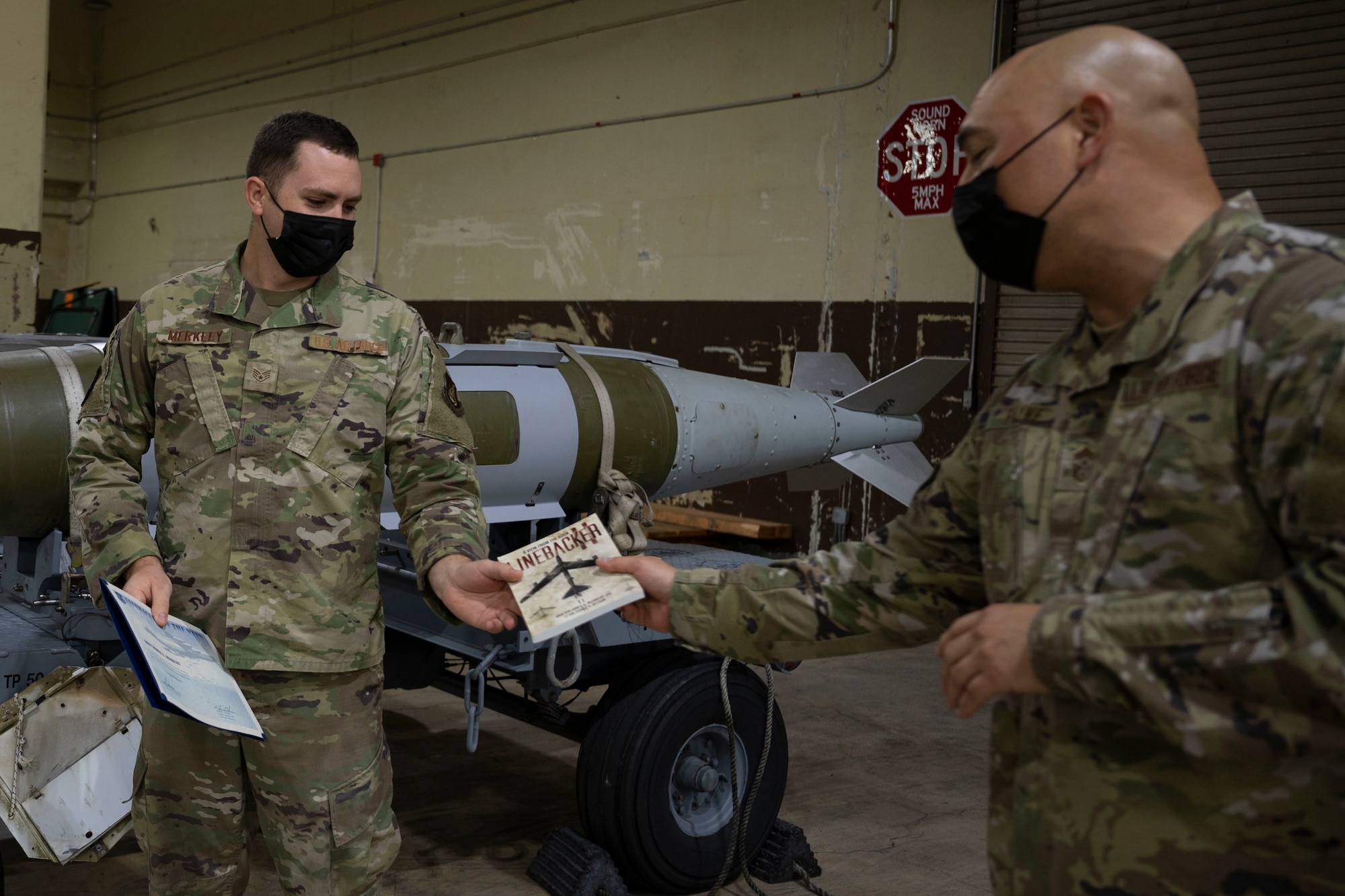 U.S. Air Force Chief Master Sgt. John Payne, 36th Wing command chief, gives Staff Sgt. Derek Merkley, Munitions Support Equipment Management crew chief with the 36th Munitions Squadron, a book about the history of Operation Linebacker II at Andersen Air Force Base, Guam, Jan. 12, 2022.
