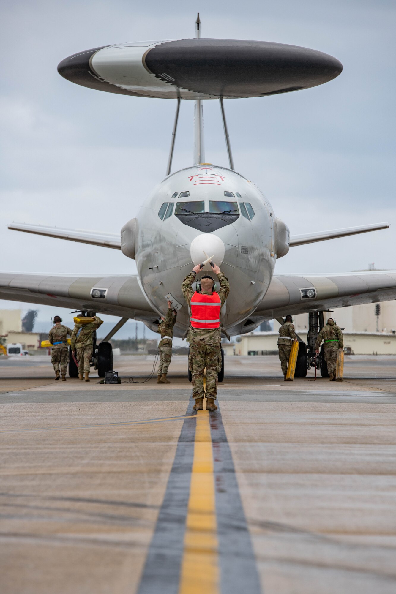 A plane stops on the flight line in front of airmen in charge of place chocks under the plane