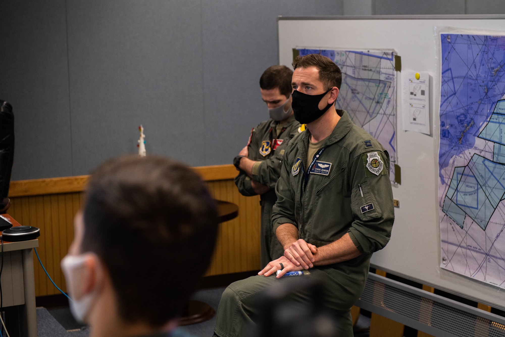 Two military members stand in front of a whiteboard planning an exercise