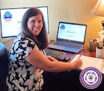 A woman sits at a desk posing for a photo in front of monitors displaying the logo for the Defense Logistics Agency and "We are DLA." At the bottom left is a logo for DLA Troop Support Office of Continuous Process Improvement.