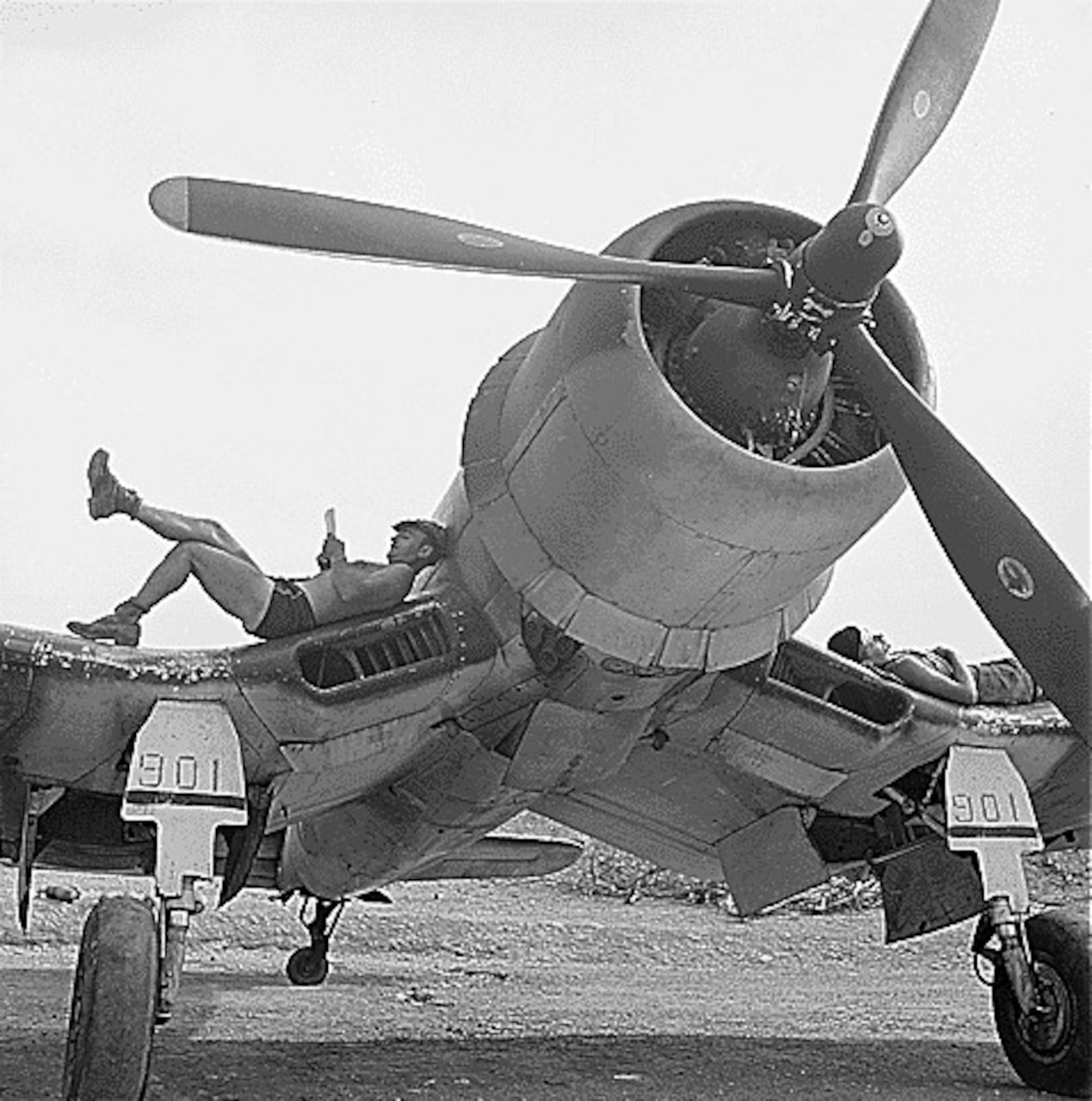 Two men lie on the wings of a propeller aircraft.