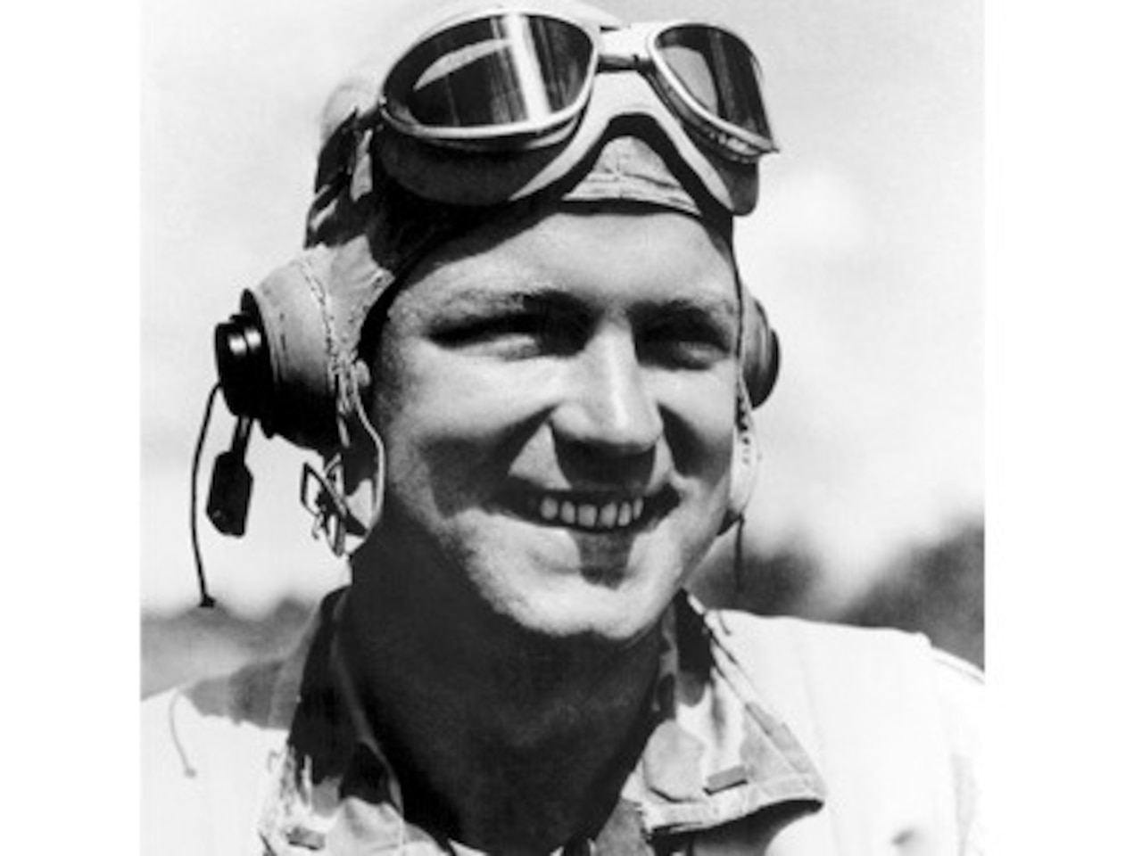 A man with aviator goggles on his forehead smiles.