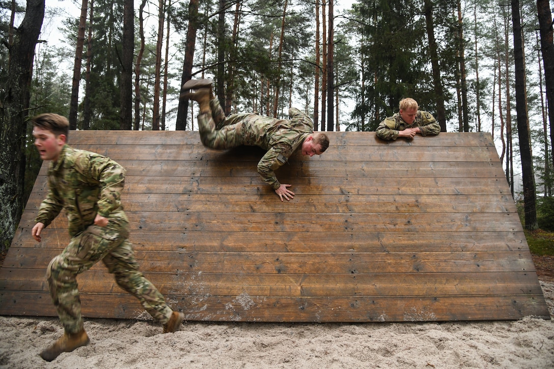 Paratroopers climb over a slanted wooden wall.